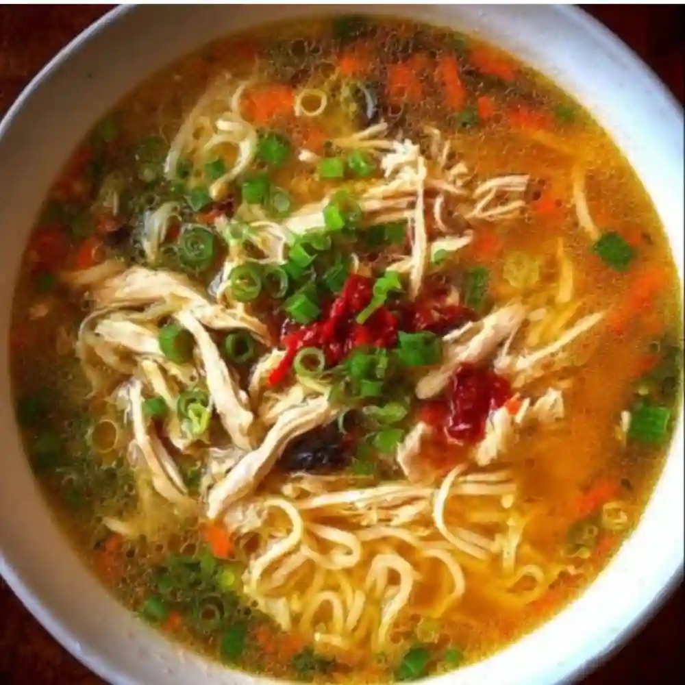 Bowl of Classic Ginger Garlic Chicken Noodle Soup garnished with herbs.