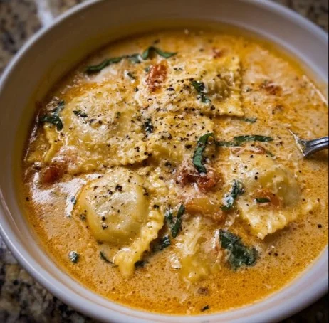 Bowl of creamy Tuscan Ravioli Soup garnished with fresh herbs.