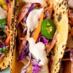 Plate of delicious cod fish tacos with fresh toppings and lime wedge.