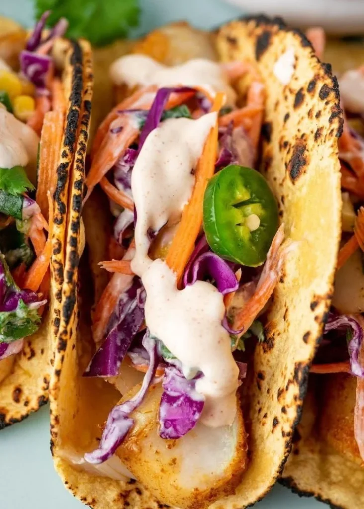 Plate of delicious cod fish tacos with fresh toppings and lime wedge.