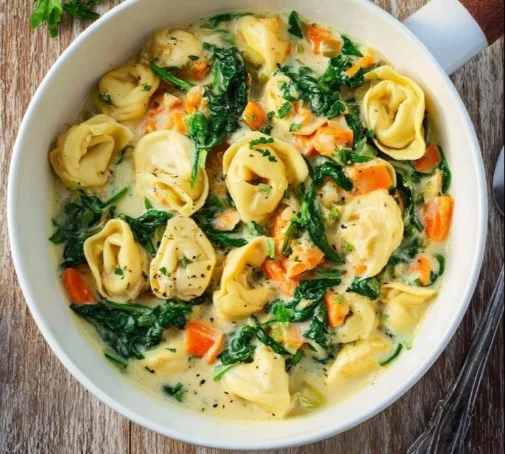 Delicious creamy chicken tortellini soup garnished with herbs.