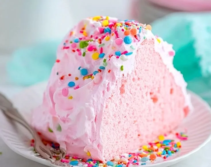 Slice of fluffy pink angel food cake with whipped cream and berries