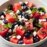 A vibrant watermelon blueberry feta salad served in a bowl, garnished with mint leaves.