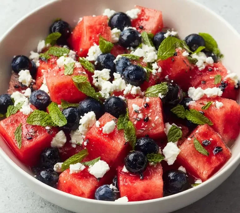 A vibrant watermelon blueberry feta salad served in a bowl, garnished with mint leaves.